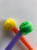 closeup of toys, looks like a solid colour straw with different colour pompoms on each end