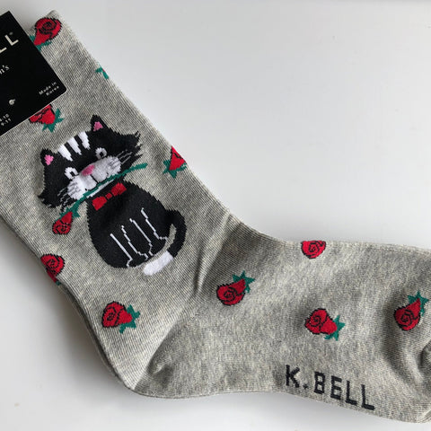 K Bell brand light grey crew sock with red roses all over it and at the ankle a black & white cat with rose in mouth