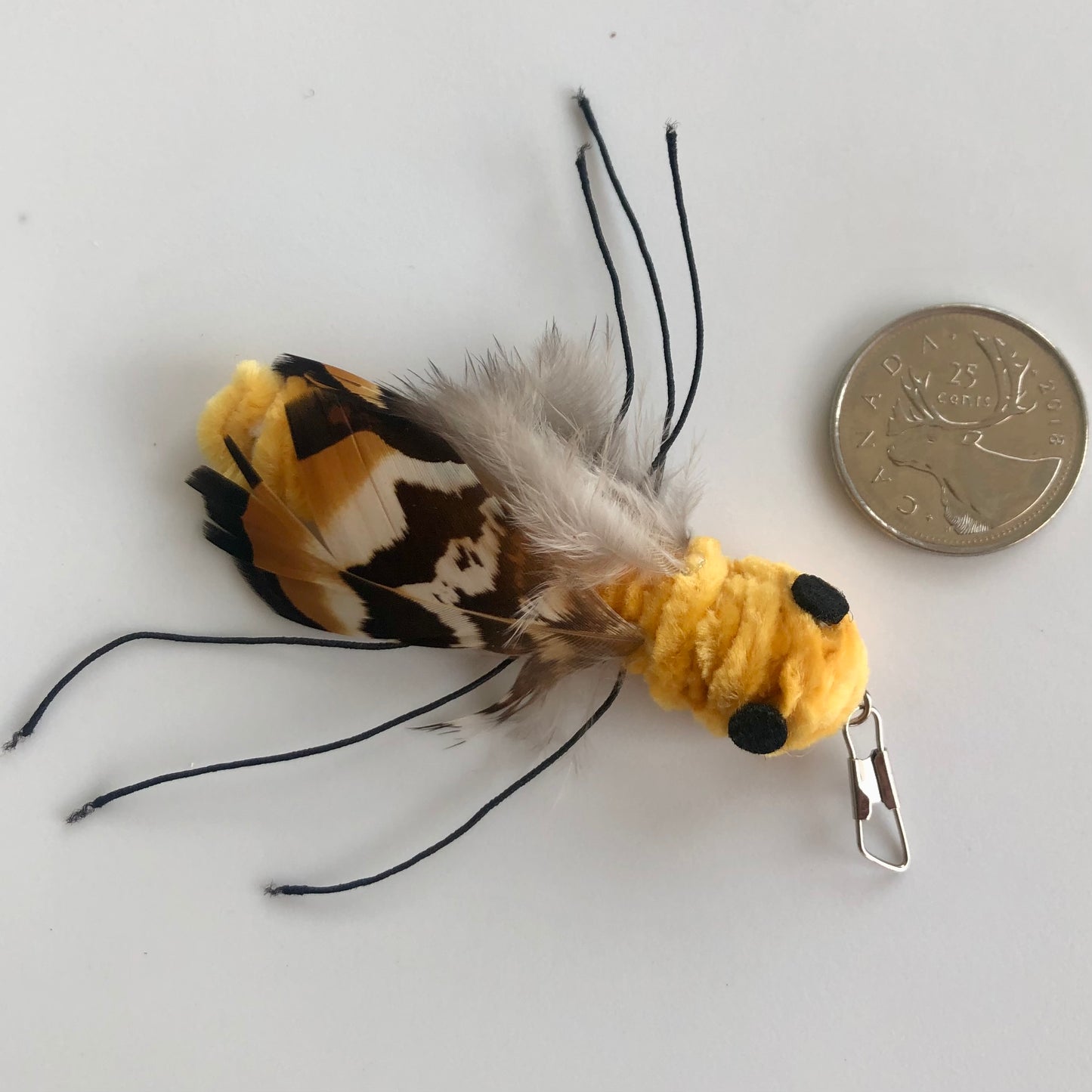 closeup of yellow and black "bug" handmade cat toy with yellow velvet velour body and brown striped feather wings, with tufts of down, shown with coin to show relative size, they come in a variety of shapes and sizes