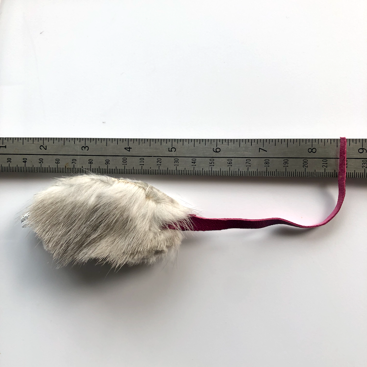 closeup of white real fur mouse with pink leather tail with ruler to measure length at about 6"; recycled fur from used fur coats.